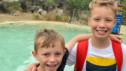 Two boys stood with their arms around each others shoulders and smiling