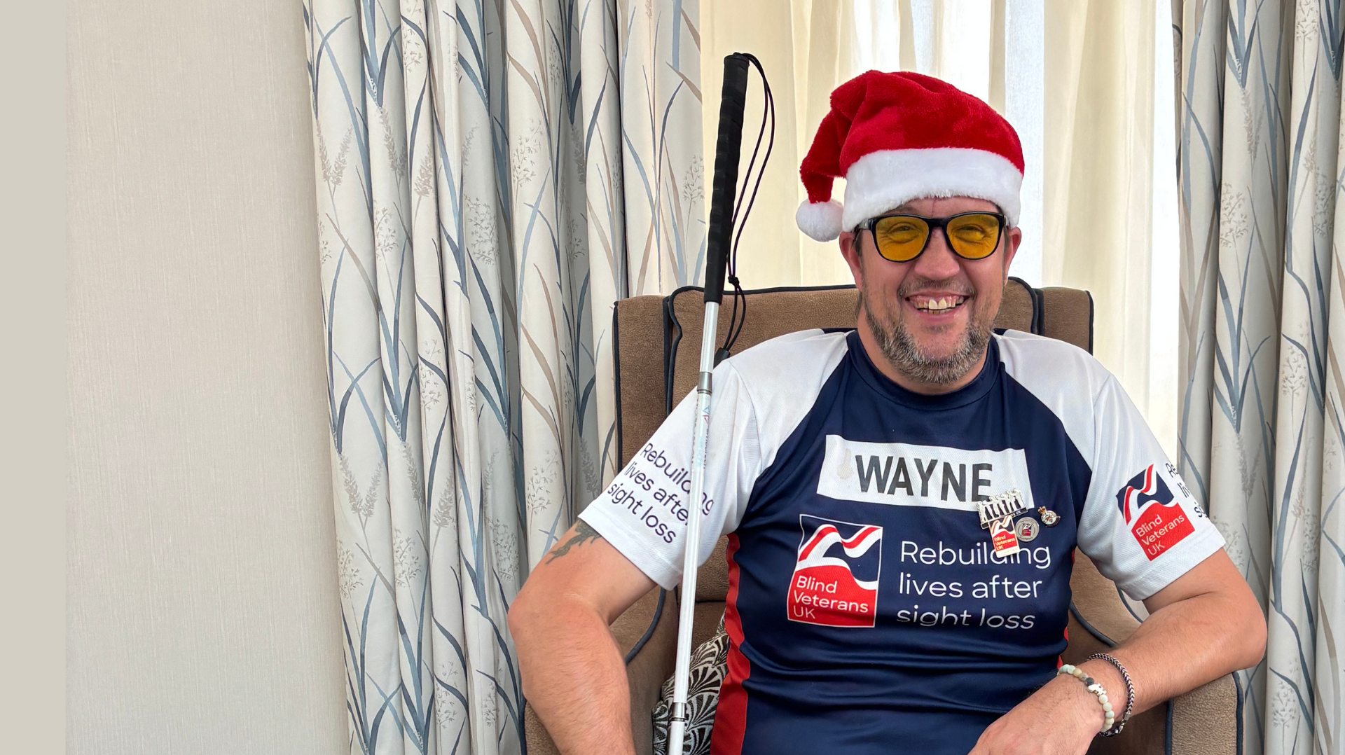 Blind veteran Wayne wearing a Christmas hat holding his cane