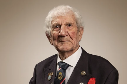 Blind veteran George in a suit wearing his medals and sitting in a chair