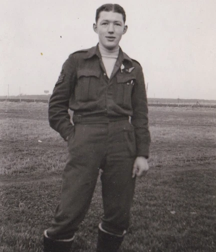 A black and white photograph of a young John, standing in a field, proudly wearing his military uniform.