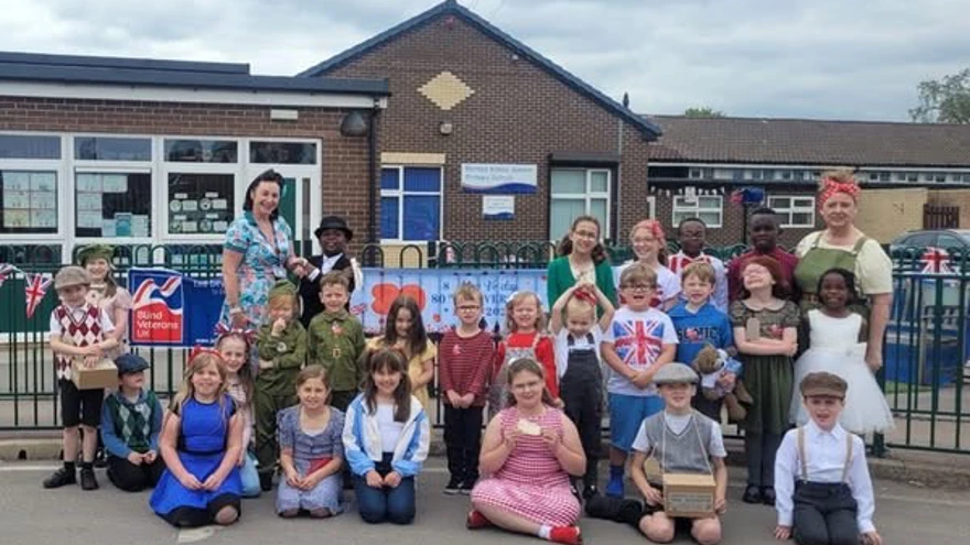 Children and staff pictured with the school in the background wearing party clothes or 1940s inspired outfits