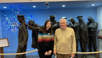 Stephanie and Mike are stood together in front of the 'Victory over Blindness' sculpture depicting a group of soldiers from the First World War leading one another away from the battlefield. Mike is holding hi white cane.