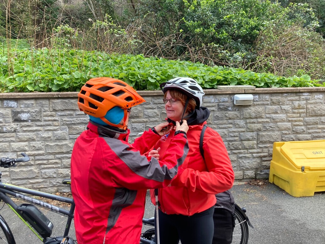 Sheila being helped to put on her cycling helmet by a member of charity staff