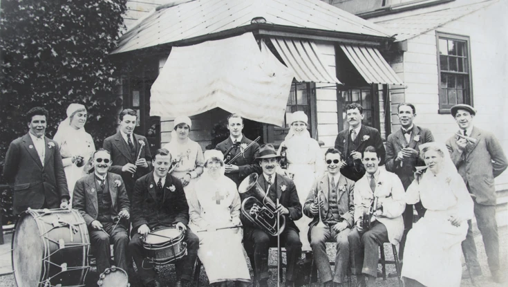 An archive group photograph of blind veterans sitting outside our old headquarters in Regents Park, holding their instruments and smiling