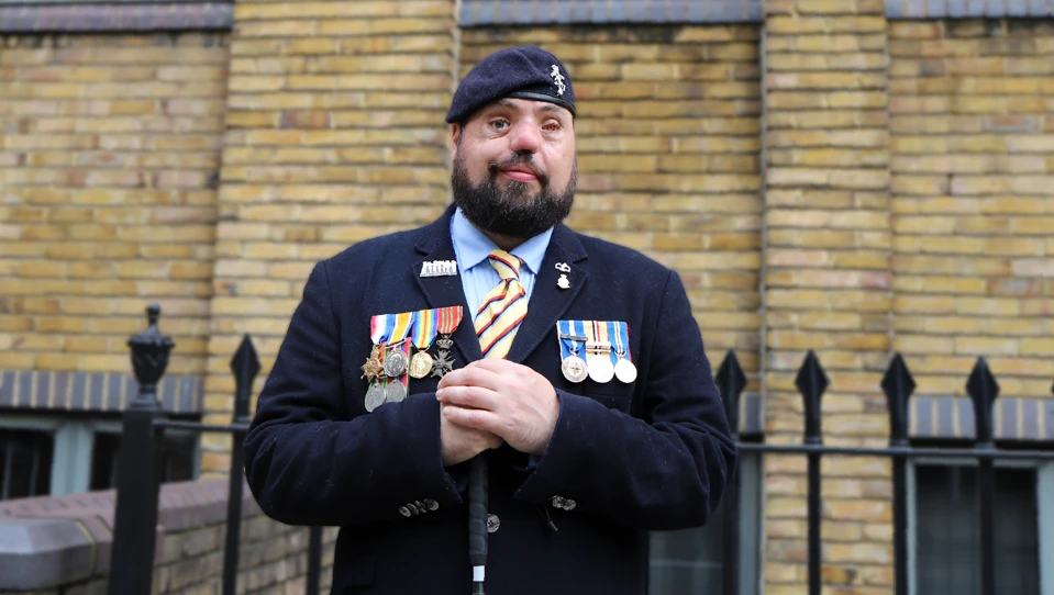 Blind veteran Simon, smiling and wearing his military uniform with badges and a beret