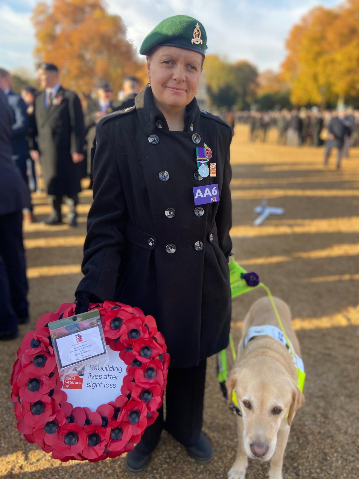 Kelly stands with the wreath in one hand and Archie's harness in the other. She is wearing a black jacket, beret and medals.