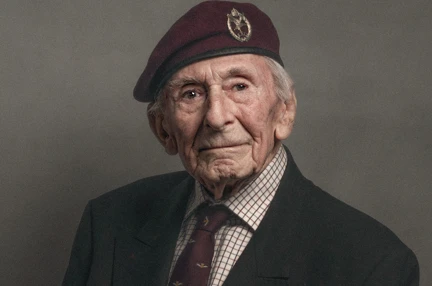 A close-up of blind veteran Jim, wearing a maroon beret with a suit and tie