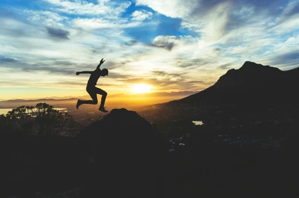 A silhouette of a person jumping across a back drop of a sunrise and mountains.