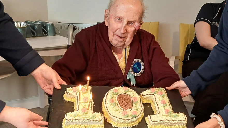 Ken looks at the camera with his very special cake in the shape of the number 101 in front of him
