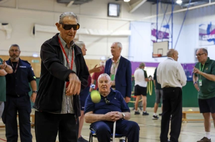 A blind veteran in dark glasses throws a tennis ball