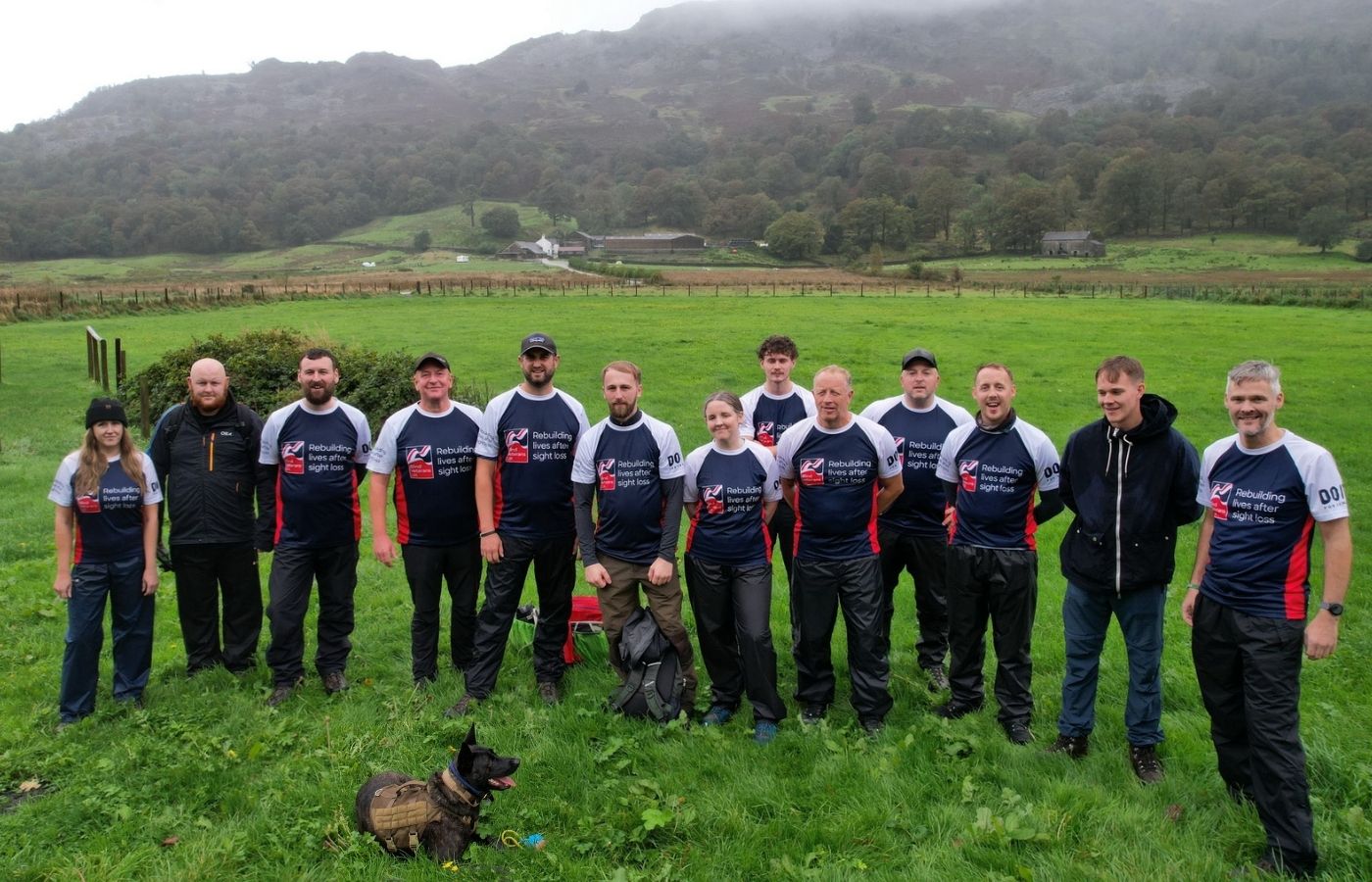 The group are stood in a field with hills behind and are wearing their Blind Veteran UK T-shirts