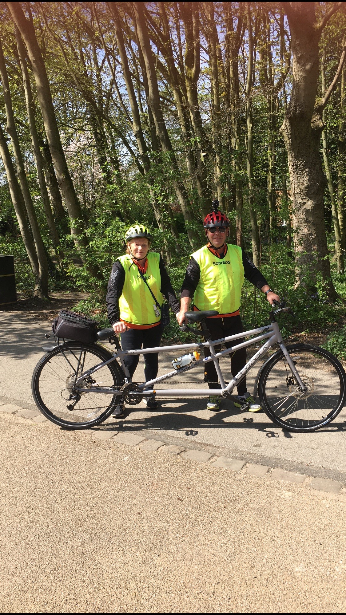 Richard and Maria dressed in high vis tops stood holding up their tandem bike