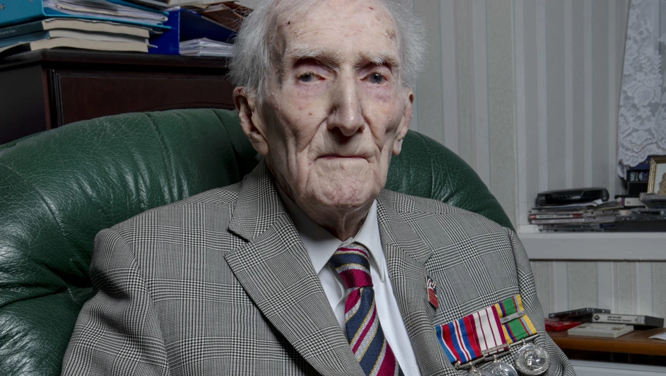 Peter sat in a chair holding a framed photo of himself in service