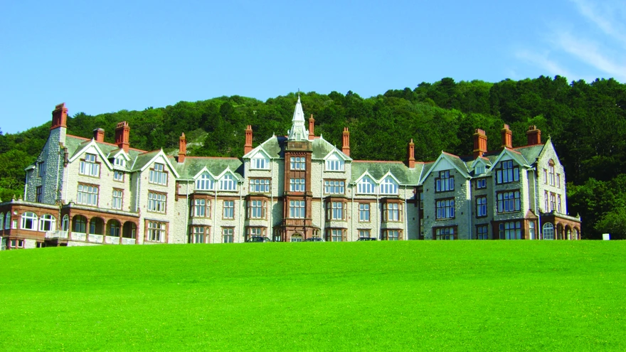 Our Llandudno Centre of Wellbeing building on a sunny day, with tall trees in the background and well kept grass at the entrance