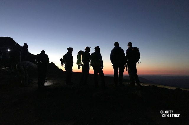 A silhouette of a group of walkers at the top of a mountain with a beautiful sunrise in the back ground.
