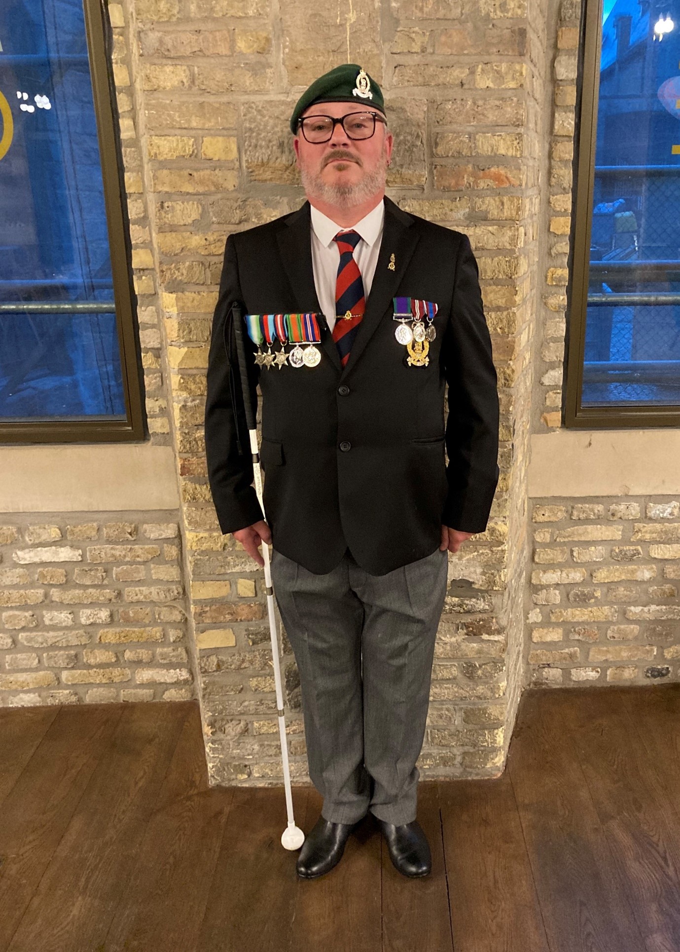 Chris in his beret and blazer and holding a white cane