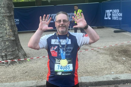 Andy has his medal around his neck and is holding up ten fingers to celebrate ten London Marathons.