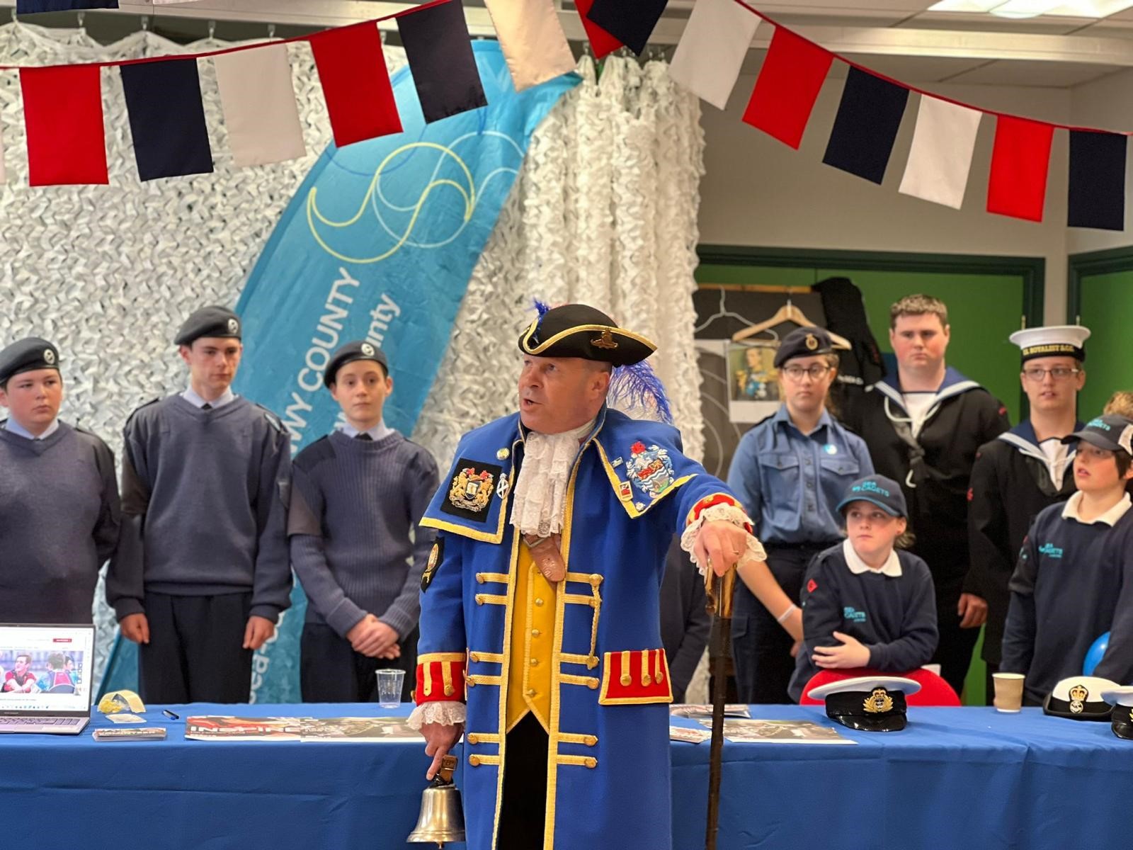 Billy in his town crier coat stood with uniformed sea cadets at their table with information leaflets about their organisation
