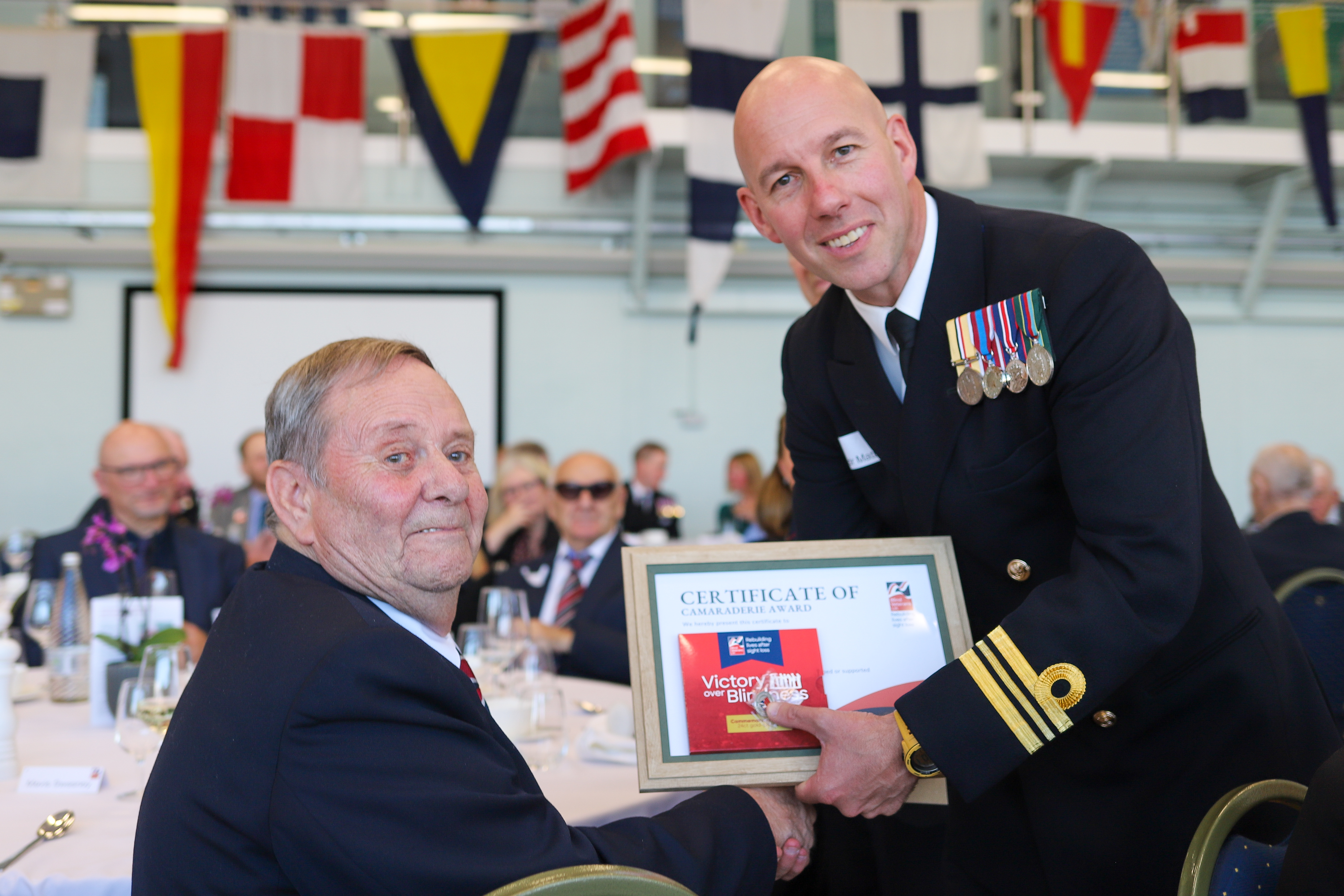 Blind veteran Brian (left) receiving his Founders Day Award from HMS Calliope Lt Cdr Matt Hulse (right).