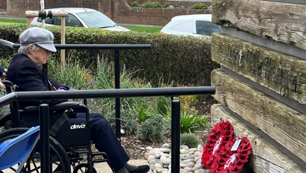 Nancy in her wheelchair reflects while looking at the wreaths laid at the war memorial