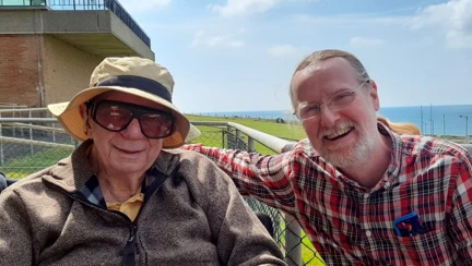 Keith and Alan are enjoying time together sat side by side with the sea in the background.