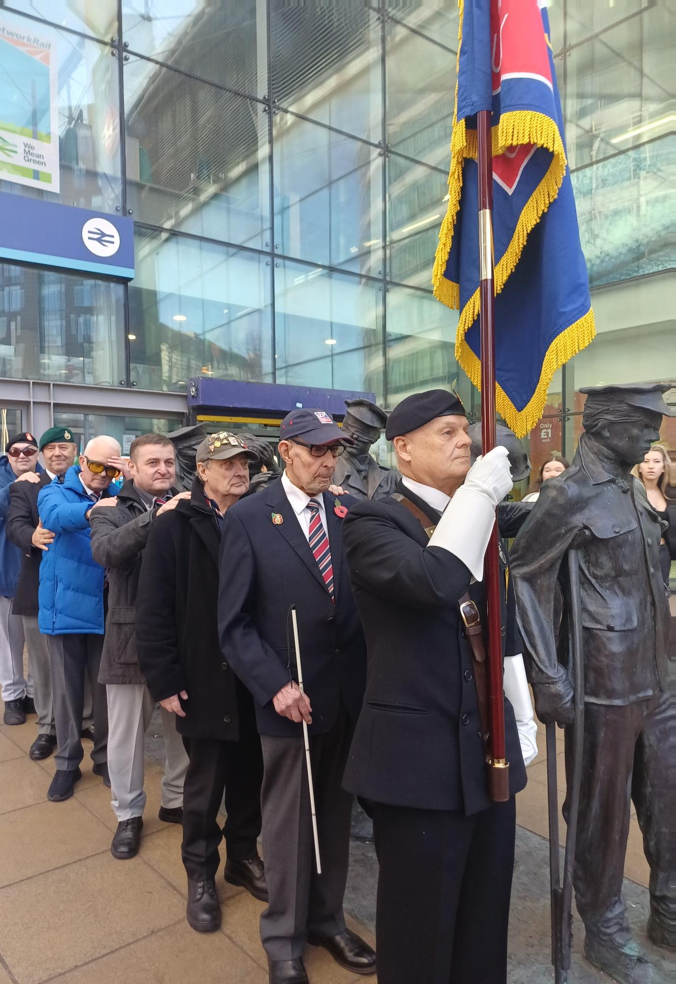 Blind veteran leads the group with his standard while the blind veterans behind put their hands on eachothers' shoulders