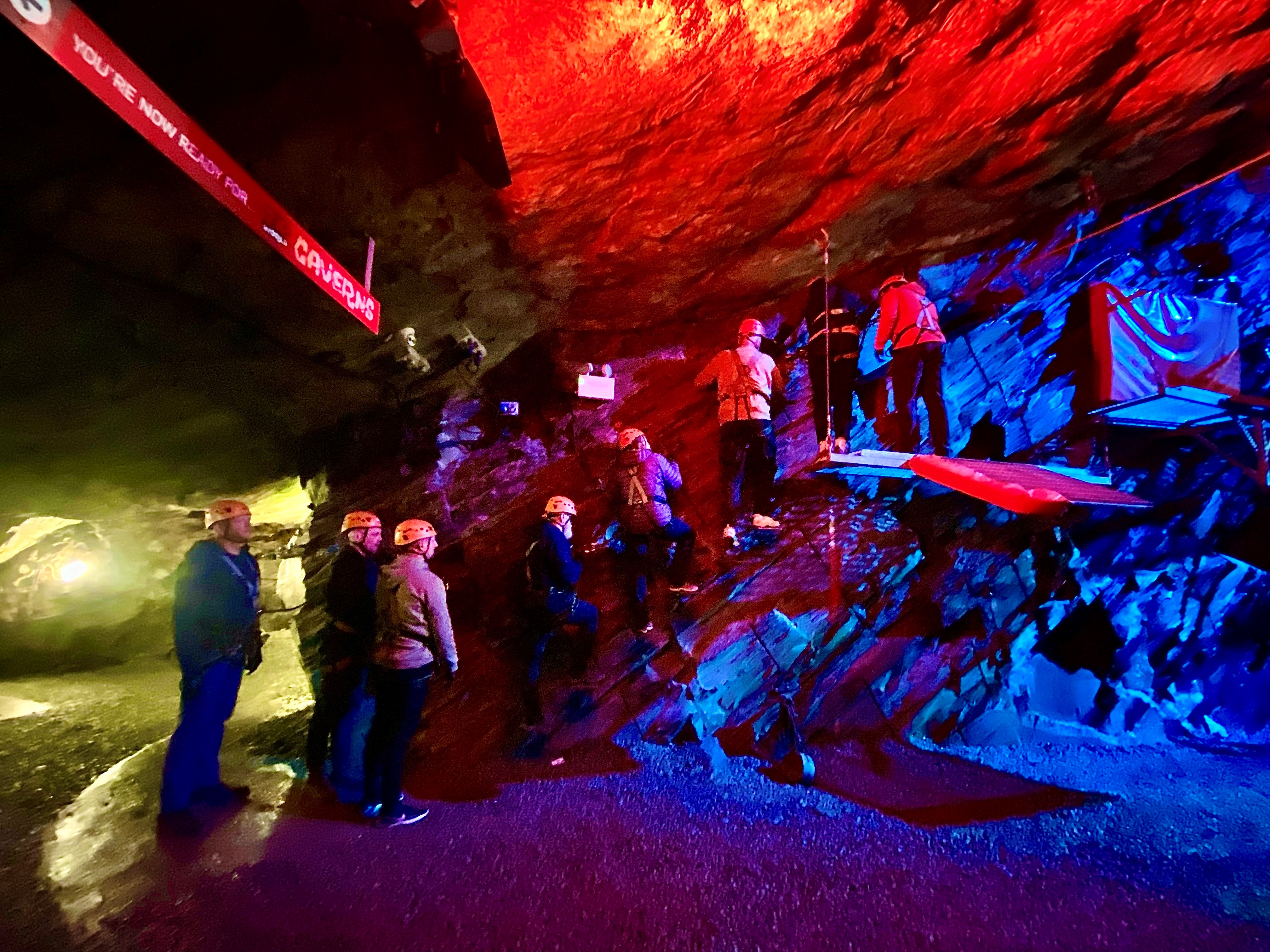 A darkly lit cavern in an old slate mine, with a group of eight blind veterans and Blind Veterans UK staff wearing helmets and harnesses as they practice climbing.