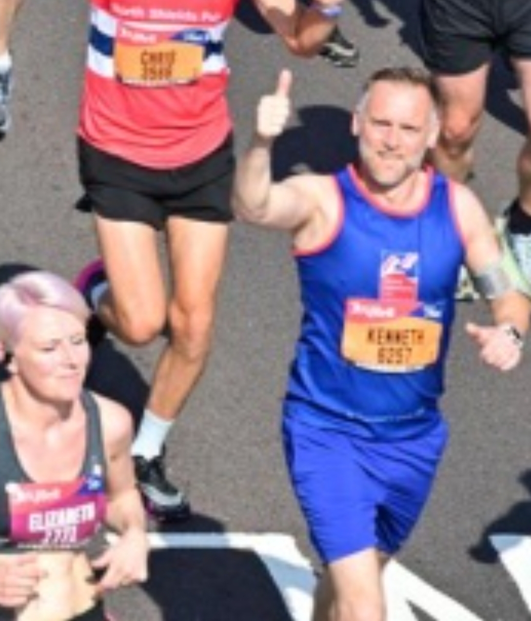 Kenny looks up for the camera while running and gives a smile and a thumbs up.