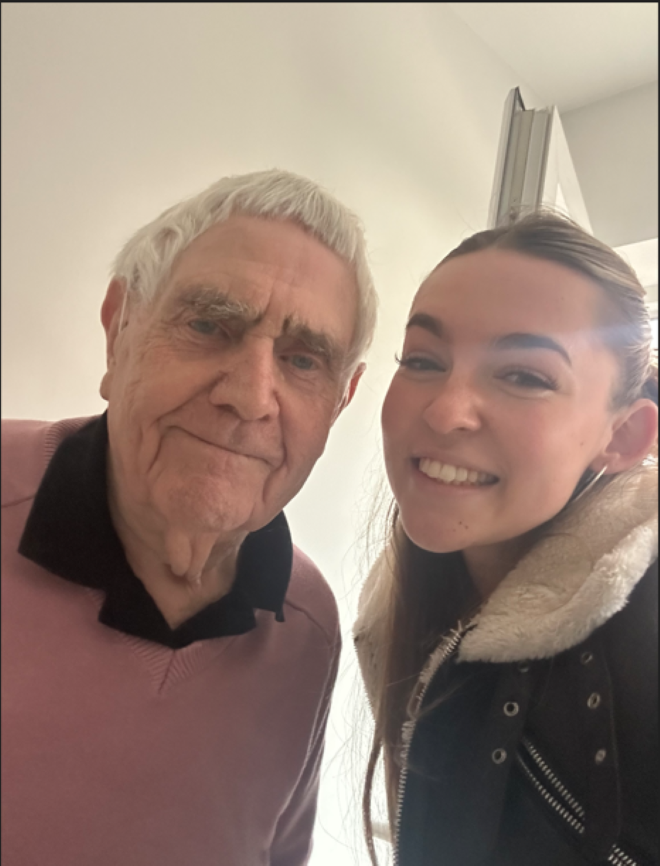 An elderly gentleman with grey hair stands next to a young lady with dark brown hair. They are looking at the camera and smiling.