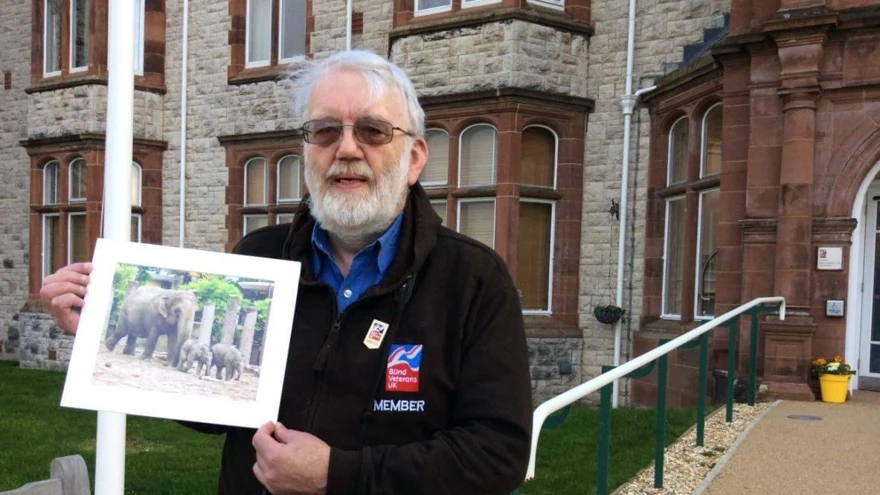 A photo of blind veteran Barrie holding up one of his photographs of an elephant and its calves