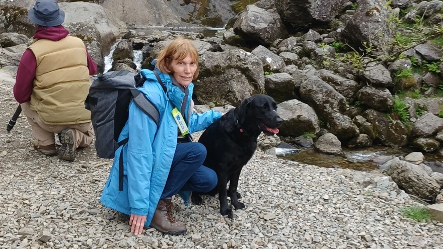 Jill with her guide dog knelt down in front of a waterfall