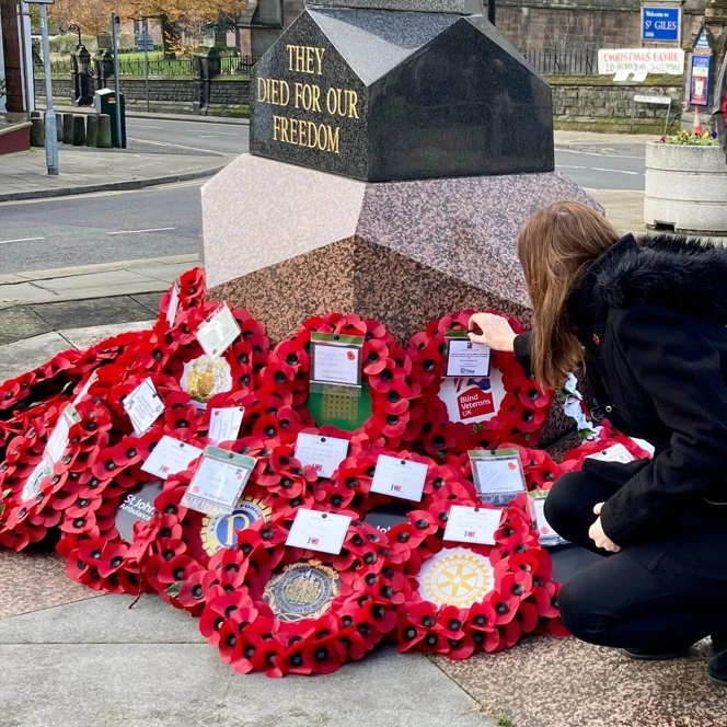 Stephanie wearing a black coat and kneeling down to place a wreath at the memorial