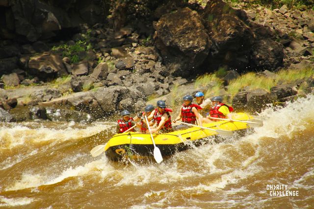 a grup of people with paddles in a bright yellow inflatable raft in the churning, white caped waters of the Zambezi river.  The rocky river bank can be seen in the back ground.