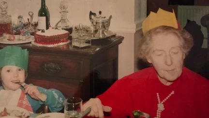 An old photograph of a young child and grandma both wearing hats from crackers and eating Christmas dinner