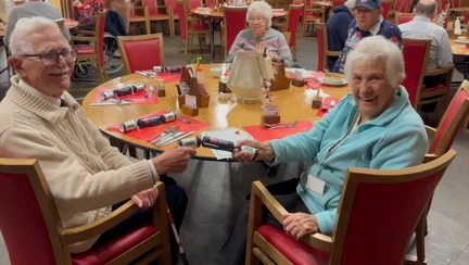 Blind veteran Nigel and his wife Antionette at a dining table at our Llandudno Centre of Wellbeing, cheerfully pulling a Christmas cracker. The table is set for a festive meal.