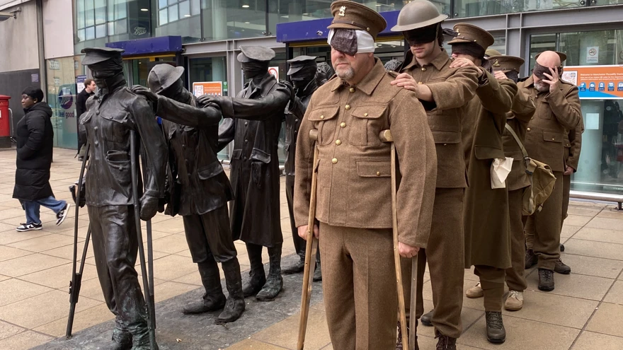 Seven men dressed in First World War army uniforms stand next to the statue of the same style