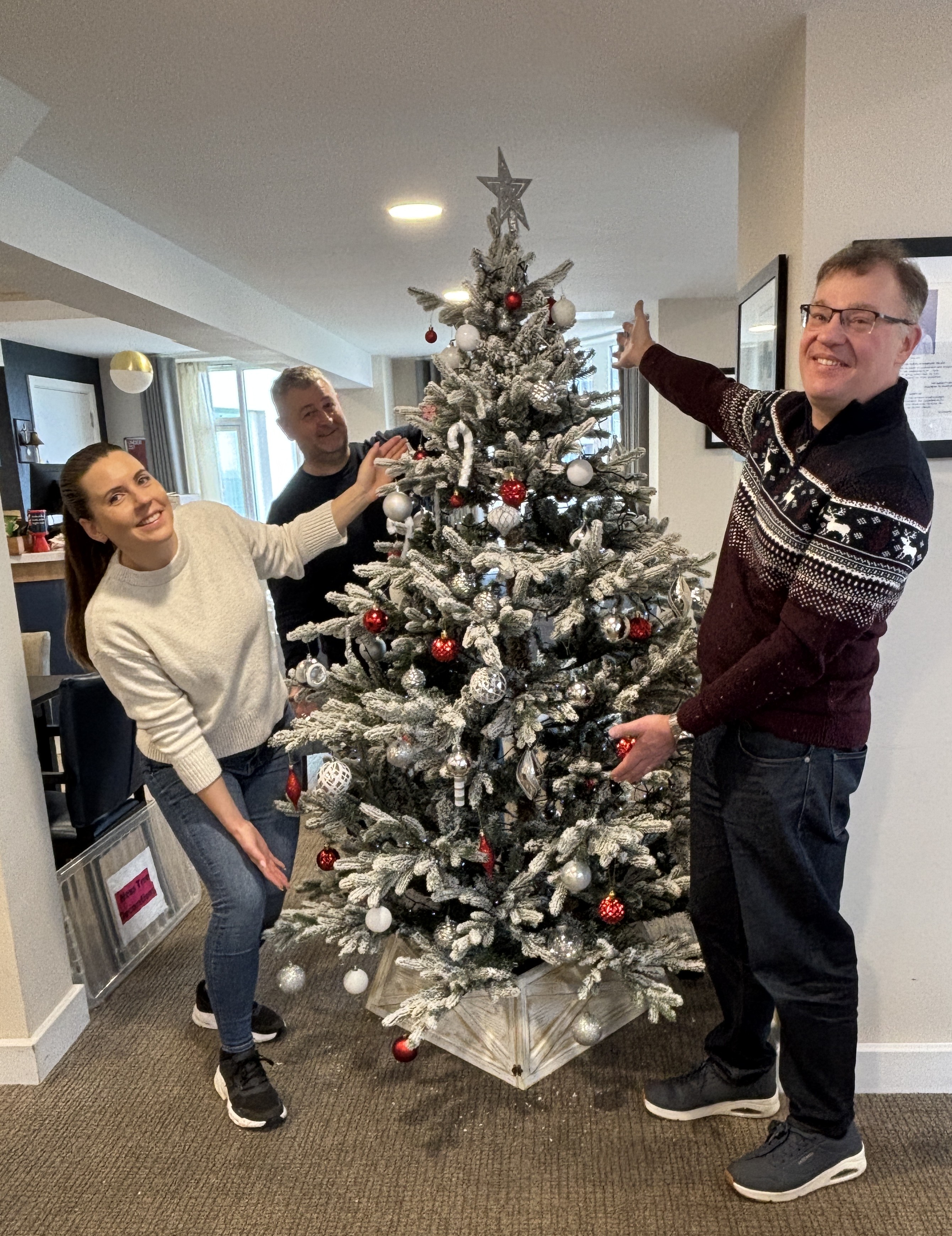 Three Sopra staff stand around a Christmas tree they have decorated and smile