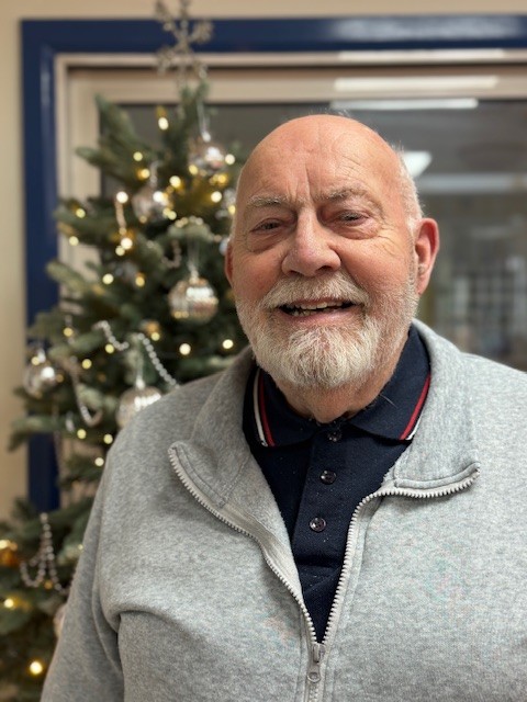Ron looks into the camera with a Christmas tree behind him