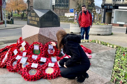 Stephanie knelt down placing a poppy wreath alongside others at a war memorial