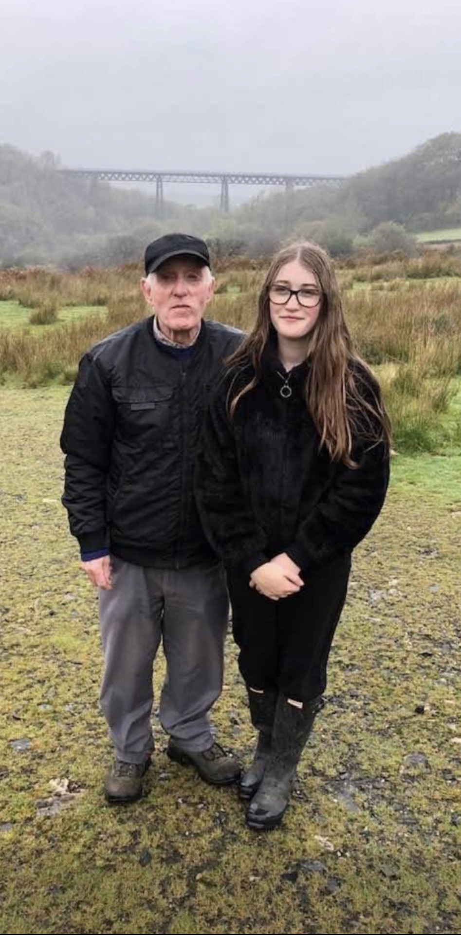 John and Lilly are stood with a bridge in the misty background. The pair are dressed up warmly complete with walking boots.
