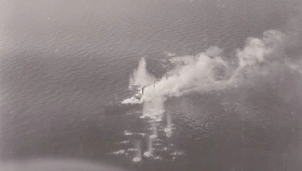 A dramatic scene from D-Day, showing an aircraft smashing into the sea near a ship, emitting a plume of smoke and water.