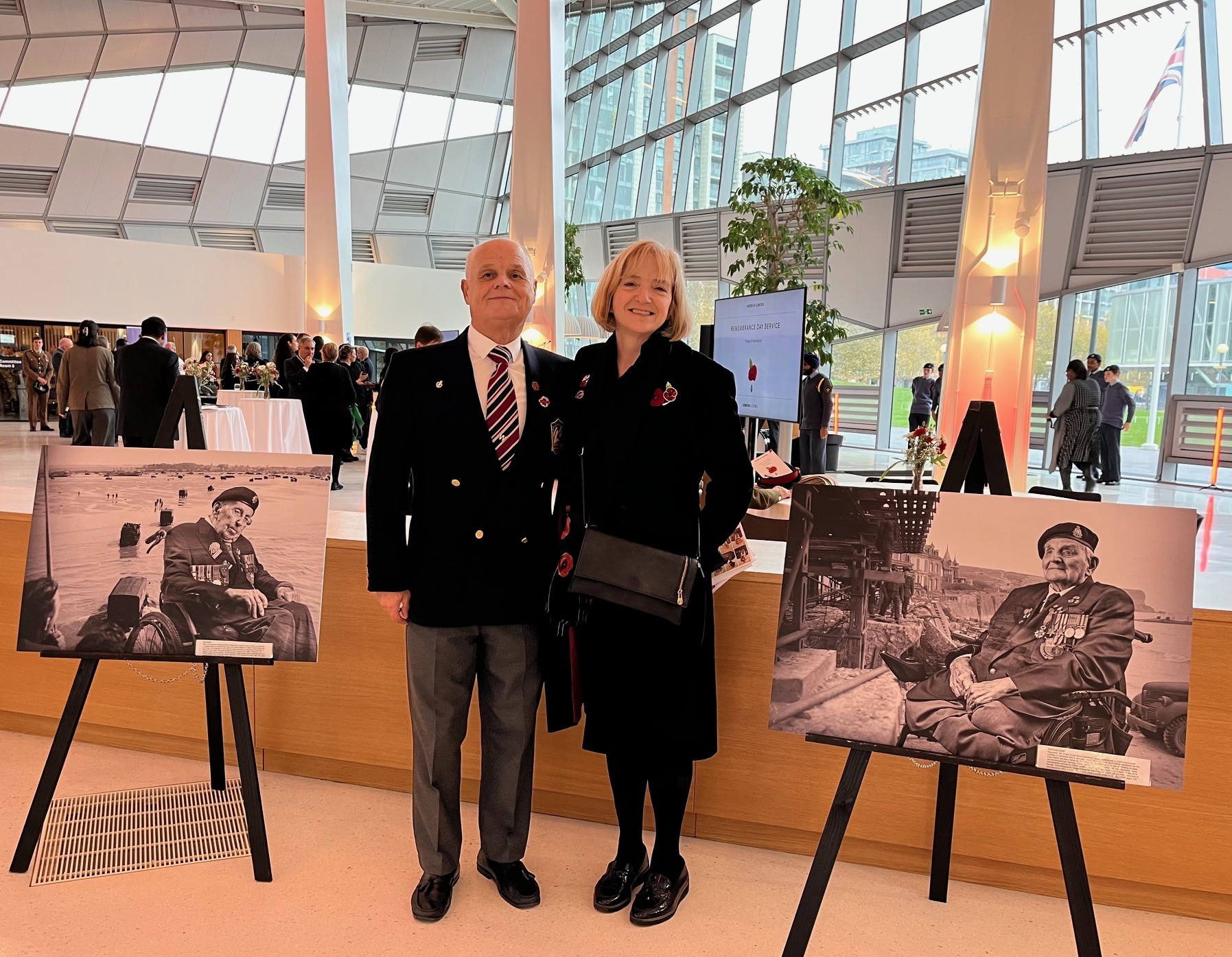 Glynis and Wayne pose for the camera, they are flanked by Blind Veterans UK D-Day portraits that are on display