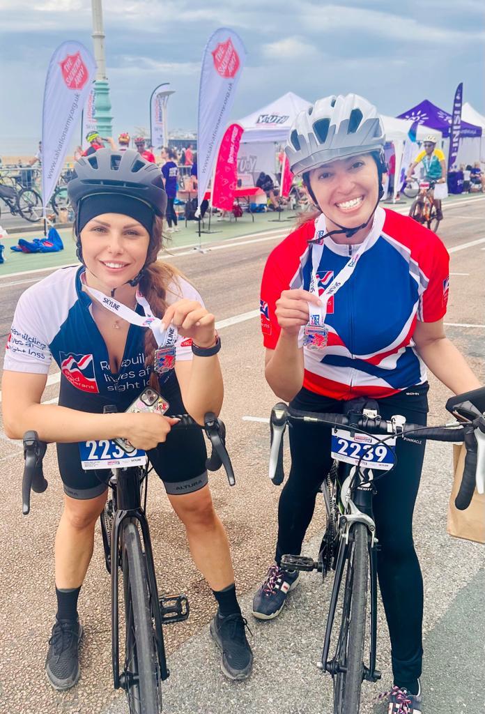 Maria and Sigil astride their bikes, smiling and holding their medals proudly at the finish line