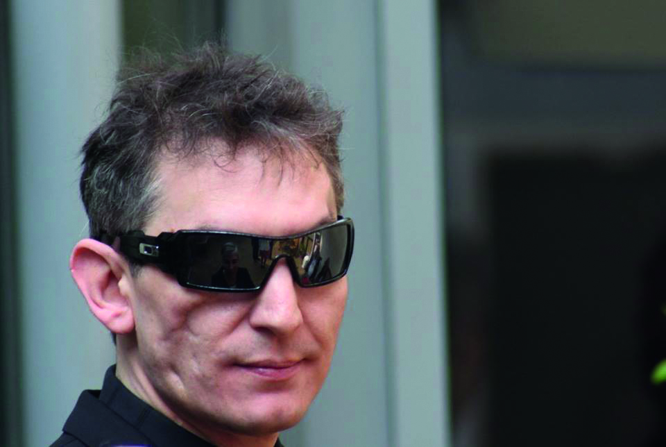 A close-up portrait of Ben wearing dark wraparound sunglasses. He is looking slightly to the side with a calm expression.