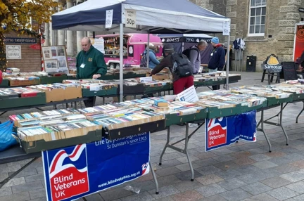 Three rows of tables set up with second hand books with two Blind Veterans UK banners hanging over the front tables