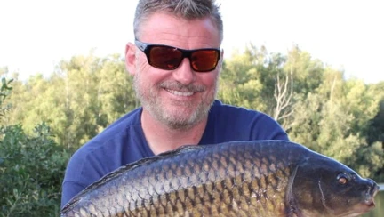 Mark kneeling down by the water holding a large carp in his hands