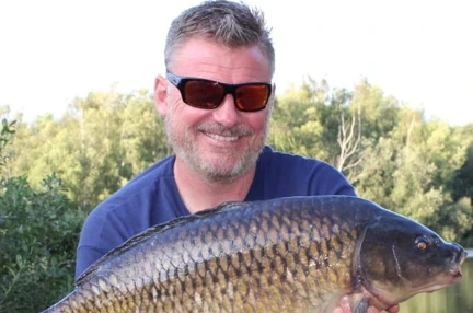 Mark kneeling down by the water holding a large carp in his hands