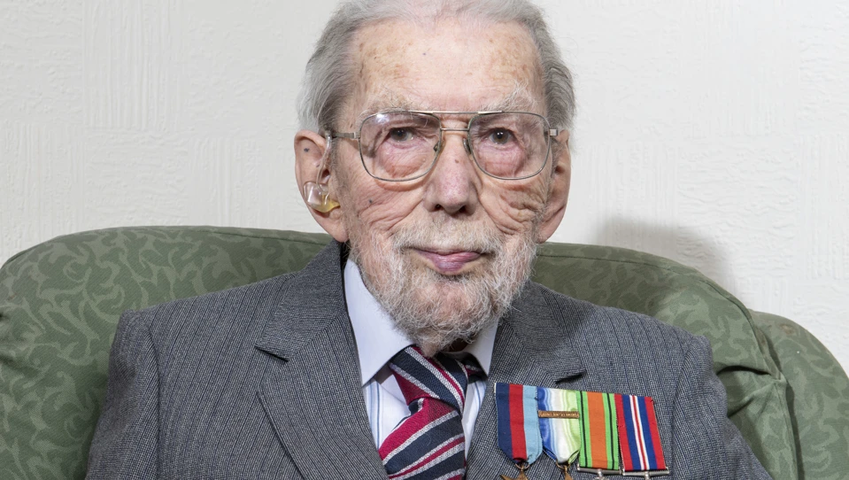 John sat in a chair holding a framed photo of himself in service