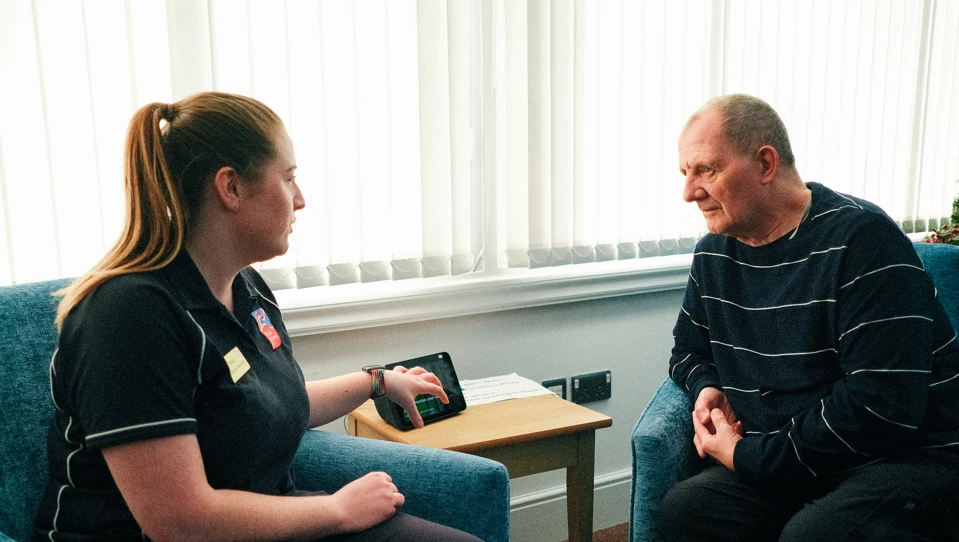 Rhian, a Wellbeing Specialist demonstrates the new Amazon Alexa at the Llandudno Centre to Blind Veteran Jules