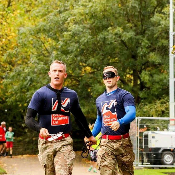 Charity supporter Nephi, running blindfolded, holding a piece of rope connected to his guide, who runs slightly ahead of him.